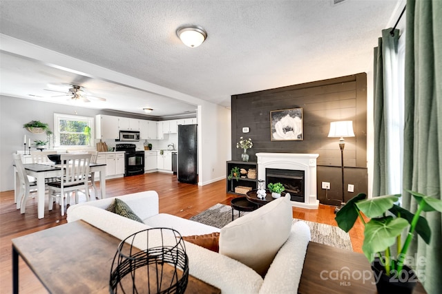 living area featuring wood finished floors, baseboards, a fireplace with raised hearth, ceiling fan, and a textured ceiling