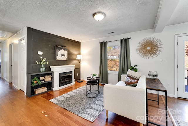 living area with wood finished floors, baseboards, visible vents, a fireplace, and a textured ceiling