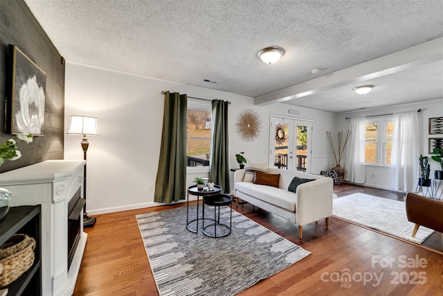 living area featuring french doors, baseboards, light wood finished floors, and a textured ceiling