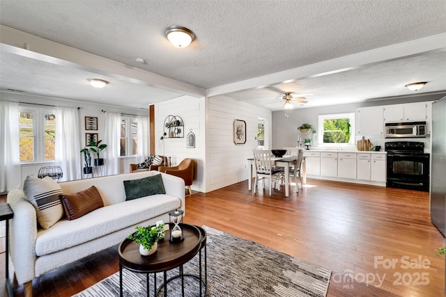 living room featuring a ceiling fan, wooden walls, wood finished floors, and a textured ceiling