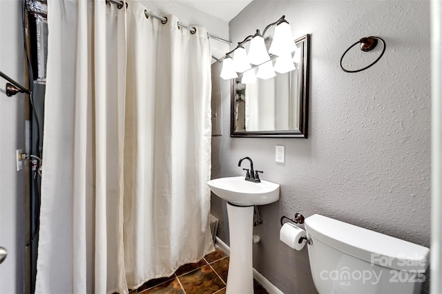 bathroom featuring baseboards, a sink, curtained shower, toilet, and a textured wall