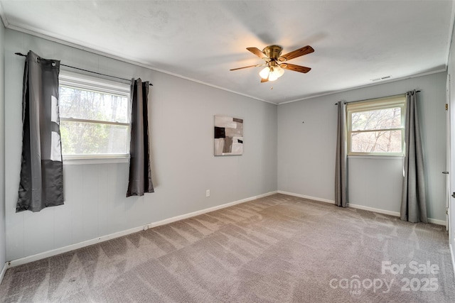 carpeted spare room with visible vents, baseboards, ceiling fan, and crown molding