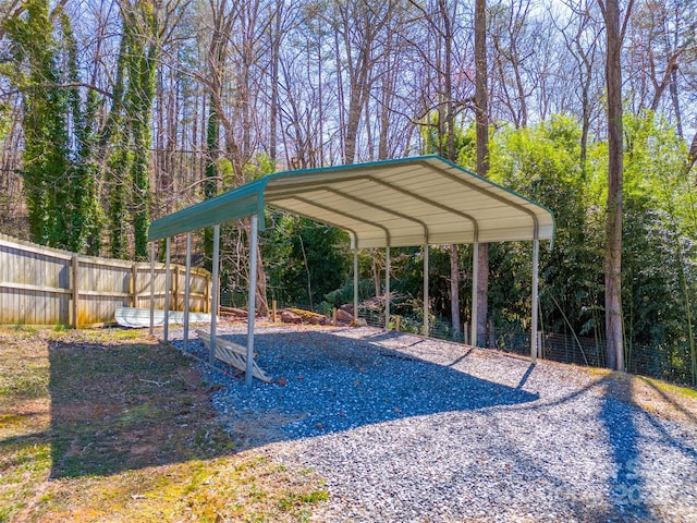 view of vehicle parking featuring gravel driveway, a detached carport, and fence