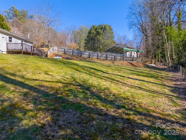 view of yard featuring a detached carport, a deck, and fence