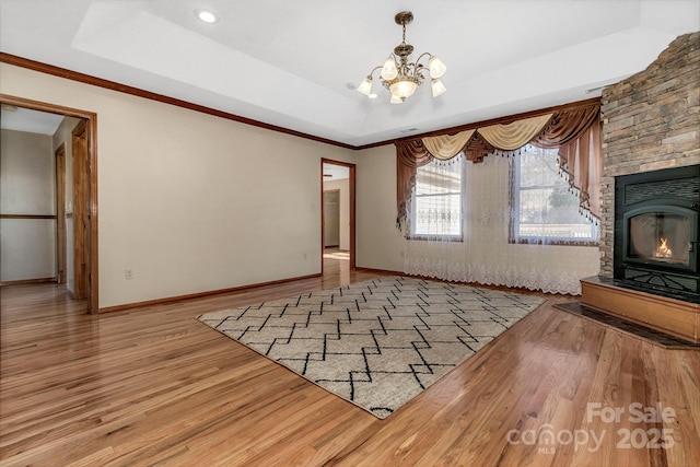 unfurnished living room featuring baseboards, wood finished floors, a notable chandelier, a glass covered fireplace, and a raised ceiling