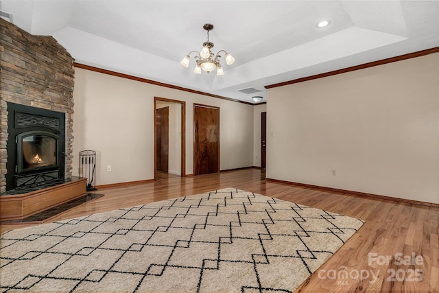 unfurnished living room featuring visible vents, a notable chandelier, a tray ceiling, wood finished floors, and baseboards