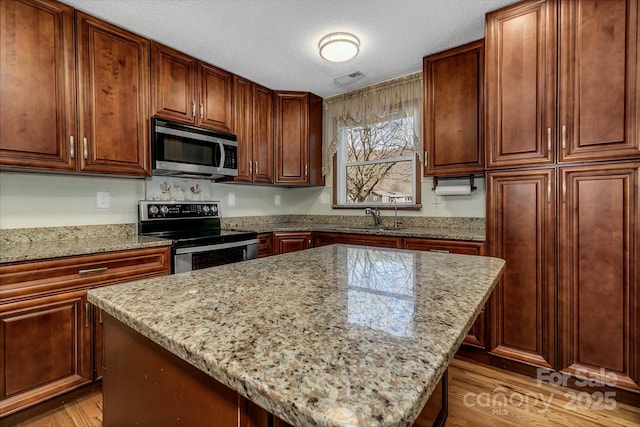 kitchen with light stone counters, appliances with stainless steel finishes, a kitchen island, and a sink