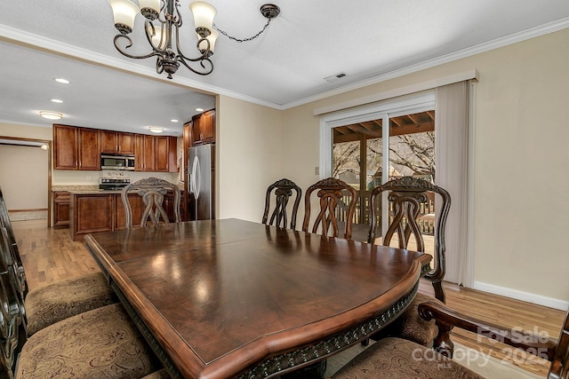 dining room featuring baseboards, visible vents, ornamental molding, light wood-type flooring, and a chandelier