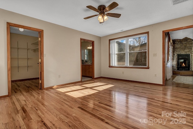 unfurnished living room featuring baseboards, visible vents, light wood finished floors, a fireplace, and ceiling fan