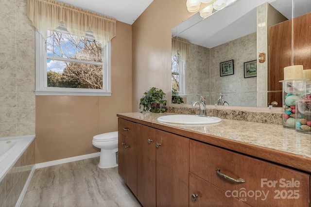 bathroom with a healthy amount of sunlight, toilet, vanity, and a relaxing tiled tub