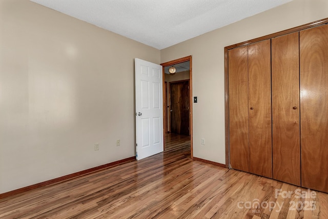 unfurnished bedroom with baseboards, a closet, light wood finished floors, and a textured ceiling