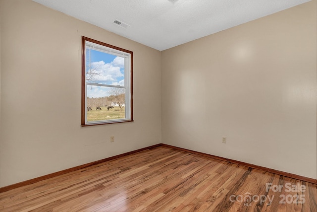 empty room featuring visible vents, baseboards, light wood-style floors, and a textured ceiling