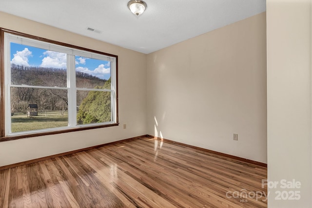 spare room with visible vents, baseboards, and wood finished floors