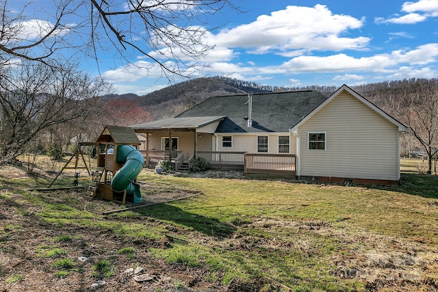 back of house with a playground, a yard, roof with shingles, and a wooden deck