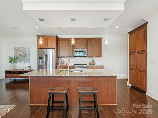 kitchen with a sink, tasteful backsplash, dark wood-style floors, appliances with stainless steel finishes, and brown cabinetry