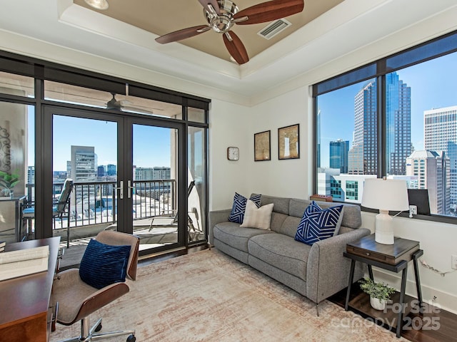 living area with a raised ceiling, a view of city, a ceiling fan, and visible vents