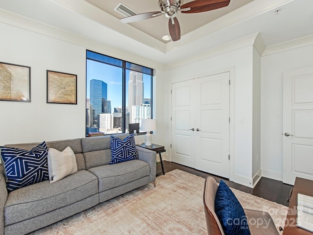 living area with visible vents, baseboards, wood finished floors, a view of city, and a raised ceiling