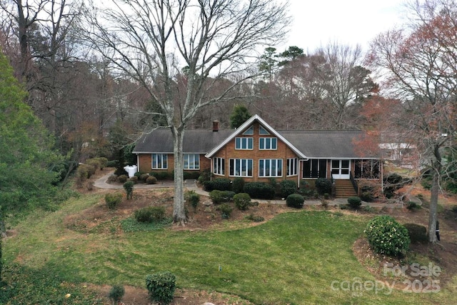 view of front facade featuring brick siding, a front yard, and a sunroom