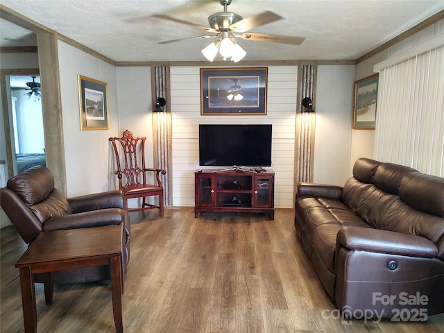 living area featuring a textured ceiling, wood finished floors, a ceiling fan, and ornamental molding