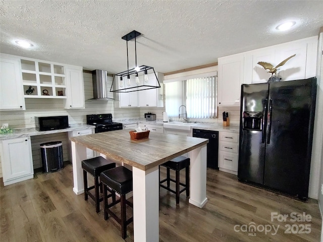 kitchen with butcher block countertops, black appliances, open shelves, a sink, and wall chimney range hood