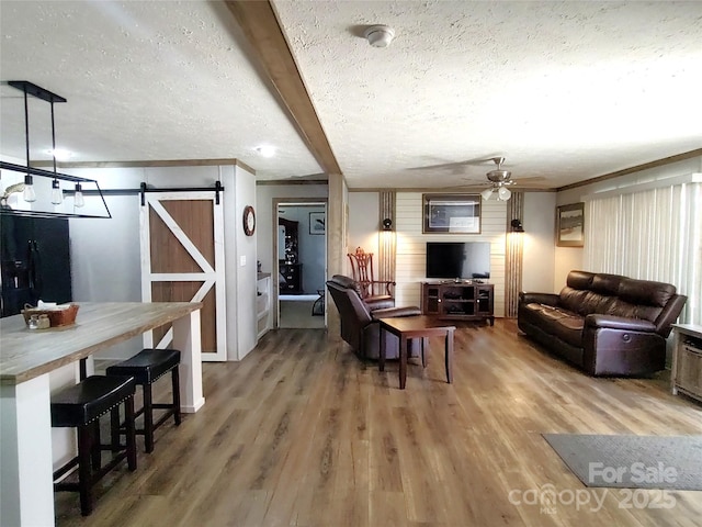 living room featuring a barn door, beam ceiling, wood finished floors, a textured ceiling, and a ceiling fan