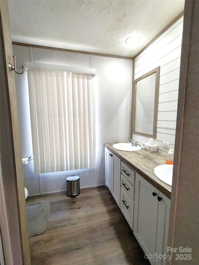 full bathroom with double vanity, a textured ceiling, wood finished floors, and a sink