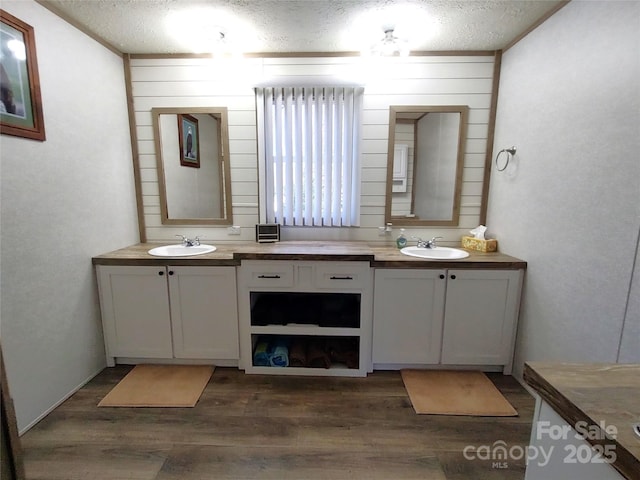 full bathroom with a textured ceiling, double vanity, wood finished floors, and a sink