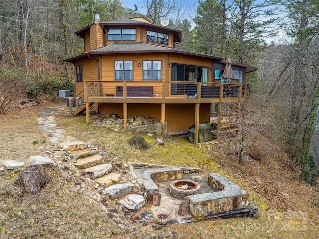 back of property with a wooded view, a wooden deck, an outdoor fire pit, stairs, and roof with shingles