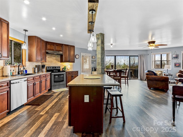 kitchen with under cabinet range hood, open floor plan, a breakfast bar, stainless steel appliances, and a sink