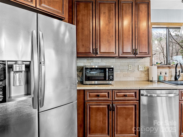 kitchen featuring backsplash, light stone countertops, stainless steel appliances, and a sink