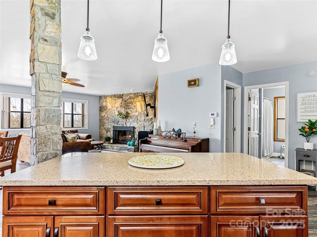 kitchen featuring a stone fireplace, pendant lighting, a ceiling fan, and a center island