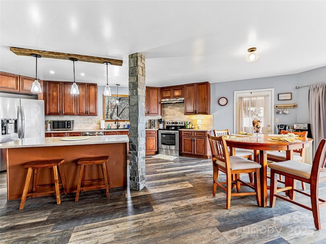 kitchen featuring dark wood-style flooring, a sink, under cabinet range hood, appliances with stainless steel finishes, and backsplash