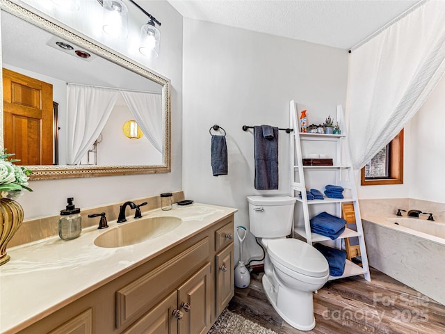 bathroom featuring toilet, vanity, a garden tub, wood finished floors, and a textured ceiling