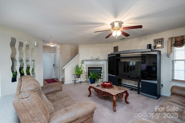 living room with baseboards, carpet, stairway, a glass covered fireplace, and a ceiling fan