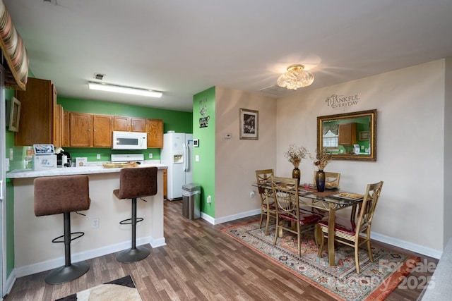 kitchen with white appliances, a peninsula, dark wood-type flooring, and brown cabinets