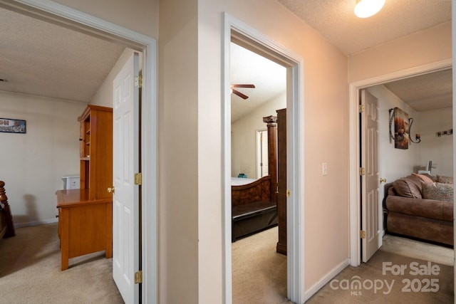 hallway featuring baseboards, a textured ceiling, and carpet