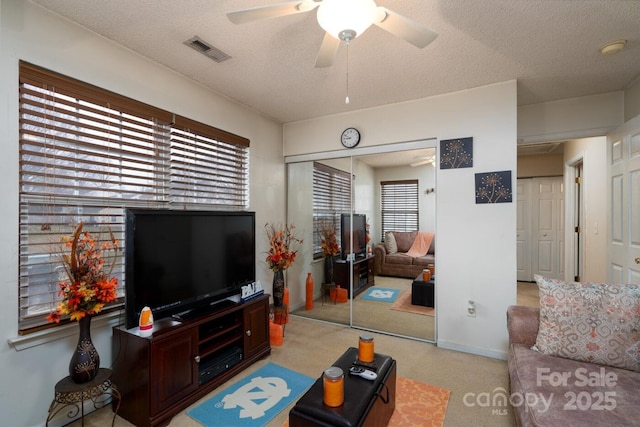 living room with baseboards, a ceiling fan, visible vents, and a textured ceiling