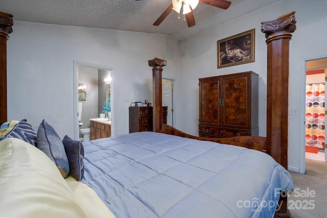 bedroom featuring a ceiling fan, ensuite bathroom, a textured ceiling, carpet flooring, and ornate columns