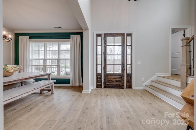 entrance foyer with a chandelier, wood finished floors, stairs, and crown molding