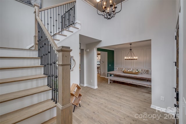 entrance foyer with a towering ceiling, stairway, light wood finished floors, baseboards, and a chandelier