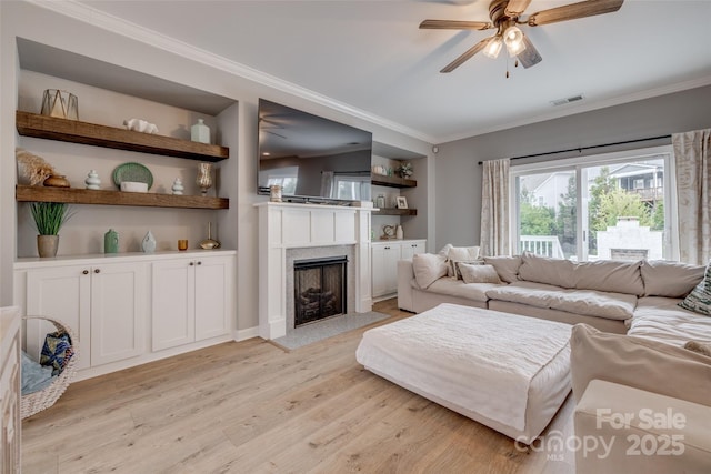 living area with light wood finished floors, built in features, a high end fireplace, and ornamental molding