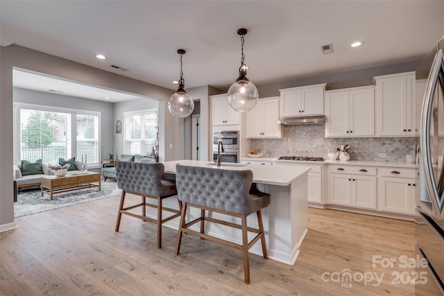 kitchen featuring visible vents, under cabinet range hood, light countertops, a kitchen breakfast bar, and stainless steel appliances