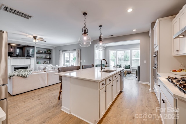 kitchen with open floor plan, visible vents, light wood finished floors, and a sink