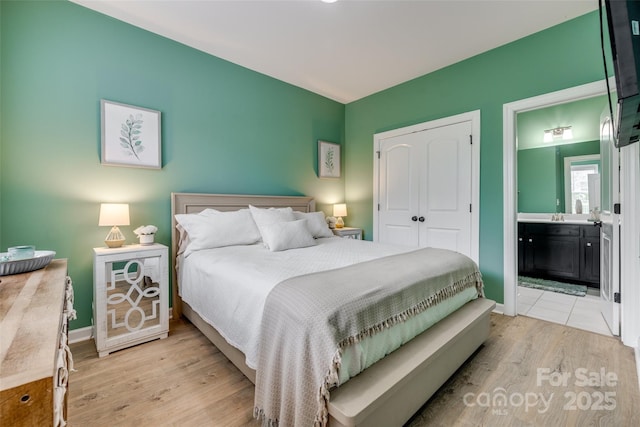 bedroom featuring a closet, ensuite bathroom, light wood-type flooring, and baseboards