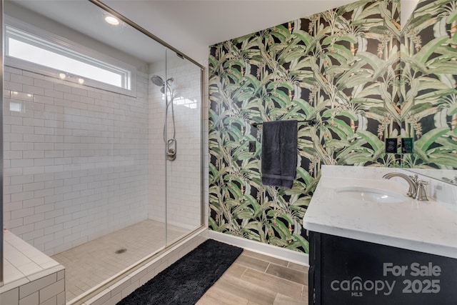 full bath featuring a shower stall, wallpapered walls, baseboards, wood tiled floor, and vanity