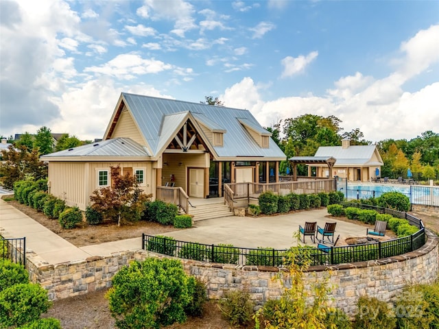 rear view of property with a patio, a community pool, fence, and metal roof