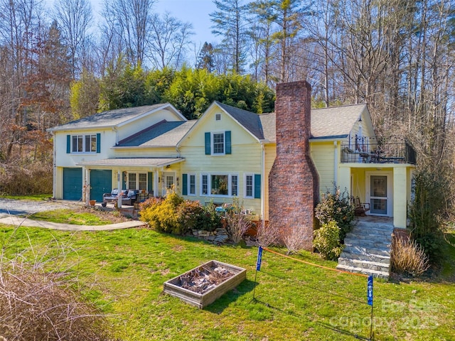 view of front of property with a front yard, a balcony, driveway, an attached garage, and a chimney