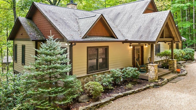 view of front of property featuring stone siding, a chimney, and roof with shingles