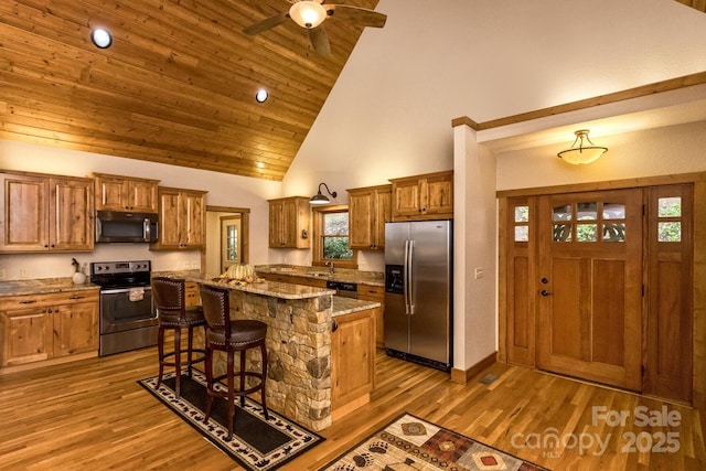 kitchen featuring wood finished floors, brown cabinetry, a kitchen island, and stainless steel appliances