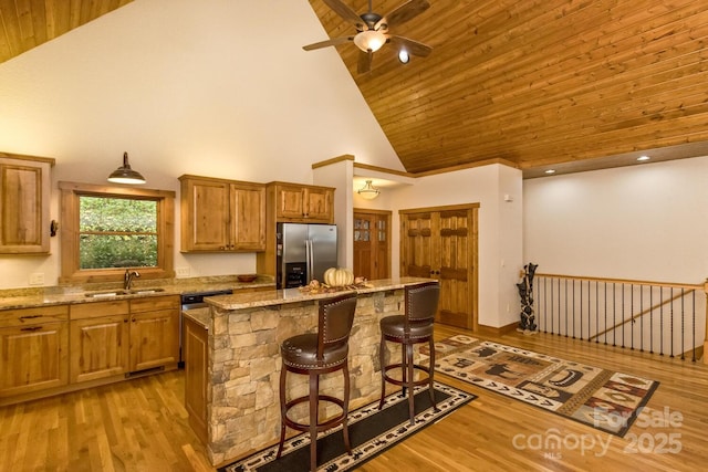 kitchen with light wood finished floors, a breakfast bar, stainless steel fridge with ice dispenser, a sink, and wooden ceiling